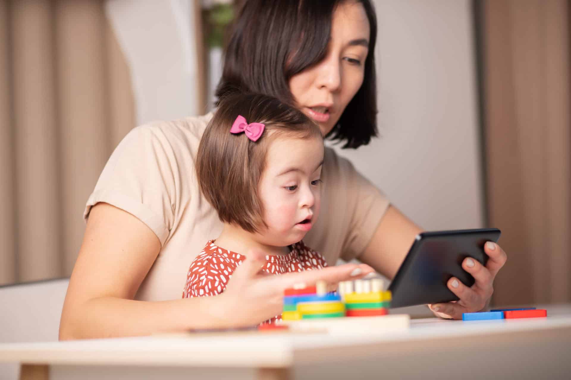 A woman holding an iPad for her young child.  They are both looking at the iPad.