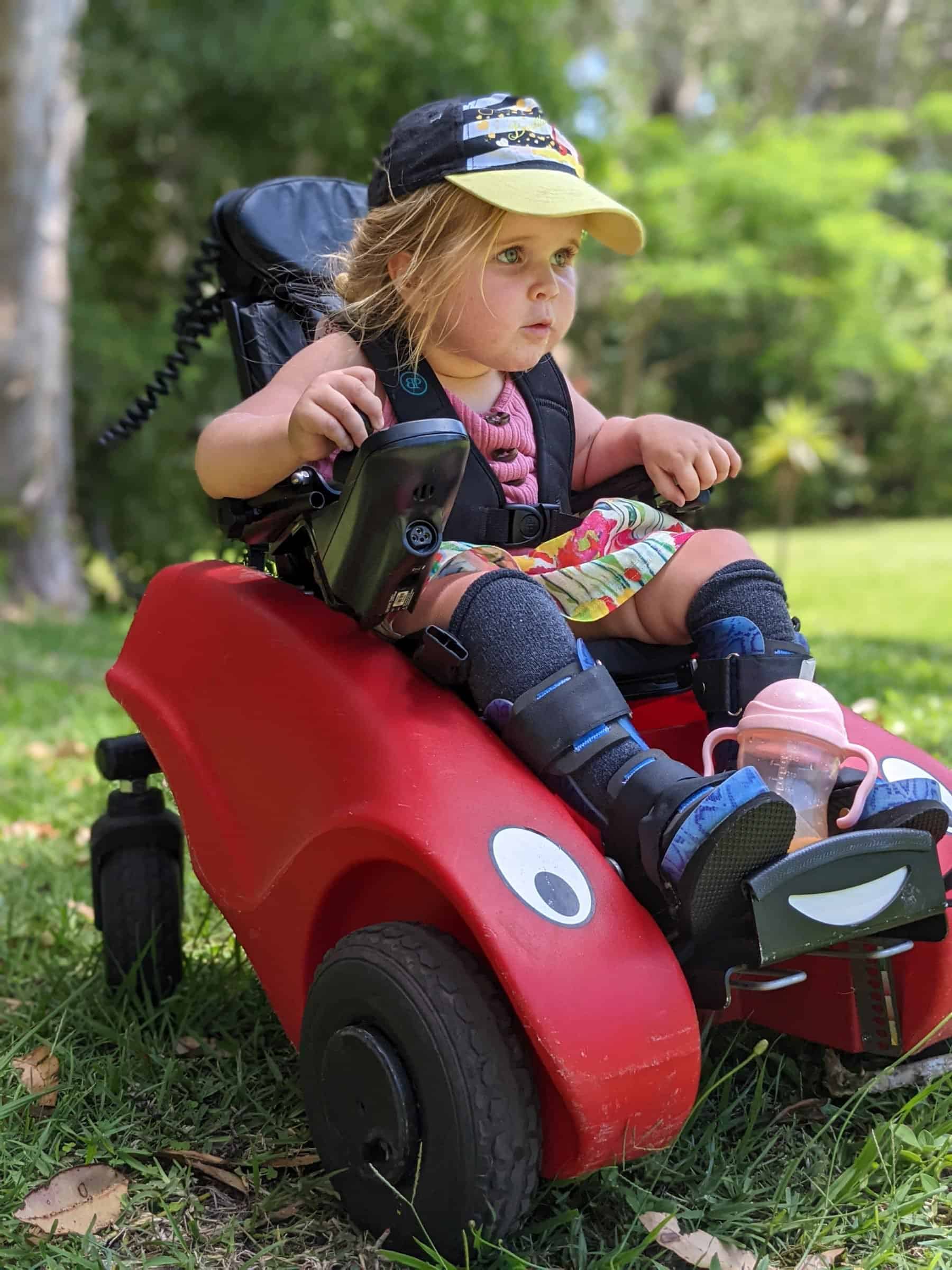 A little girl driving her Wizzybug which looks like a little red car and is powered mobility for children who cannot walk.
