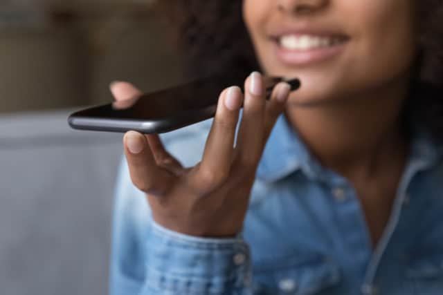 A young black woman holding an iPhone in her hand close to her face. She is speaking into the iPhone.