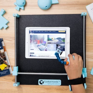 A person's hand setup in a Guided Hands assistive device. They are using the Guided Hands to access an iPad.